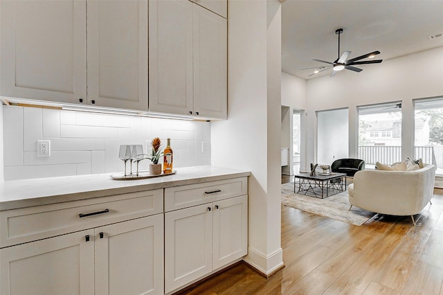 bar with visible vents, a ceiling fan, light wood-style floors, baseboards, and tasteful backsplash