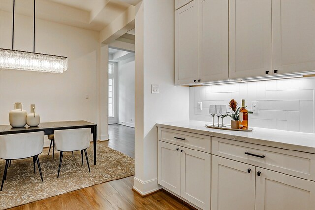 kitchen with wood finished floors, white cabinets, light countertops, backsplash, and baseboards