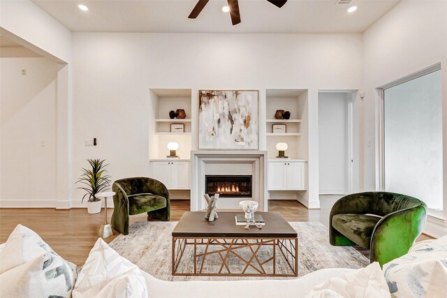 living area with recessed lighting, a warm lit fireplace, wood finished floors, a ceiling fan, and baseboards
