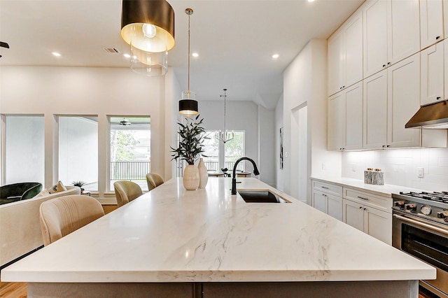 kitchen with a sink, an island with sink, high end stove, under cabinet range hood, and visible vents