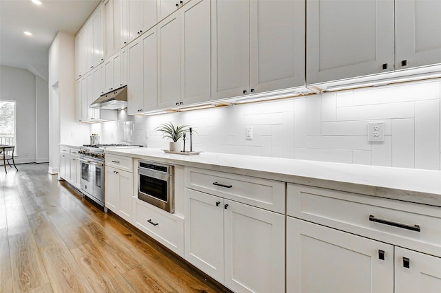 kitchen with high end range, light wood-style floors, light countertops, under cabinet range hood, and recessed lighting