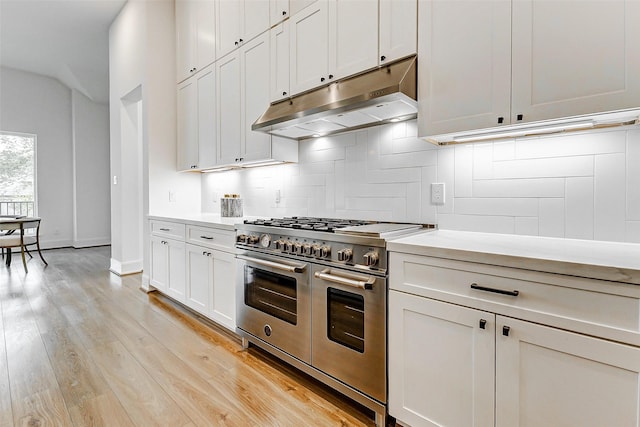 kitchen with light wood finished floors, decorative backsplash, range with two ovens, light countertops, and under cabinet range hood