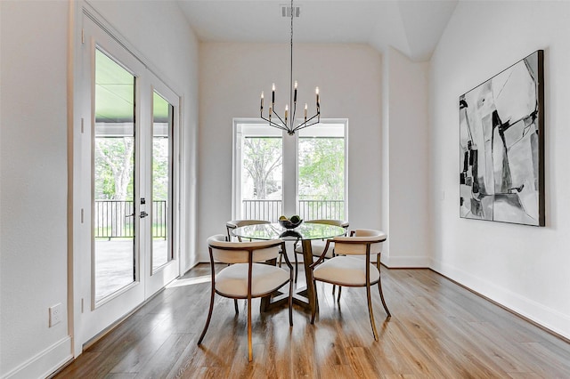dining space featuring plenty of natural light, lofted ceiling, wood finished floors, and an inviting chandelier