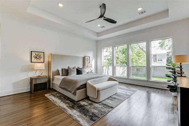 bedroom featuring a tray ceiling, wood finished floors, visible vents, and a ceiling fan