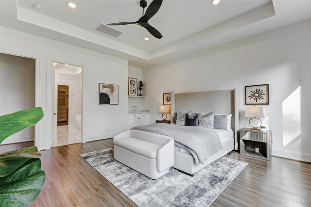 bedroom with a tray ceiling, wood finished floors, visible vents, and recessed lighting