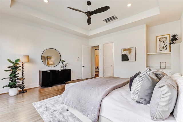 bedroom with baseboards, visible vents, recessed lighting, light wood-style floors, and a raised ceiling