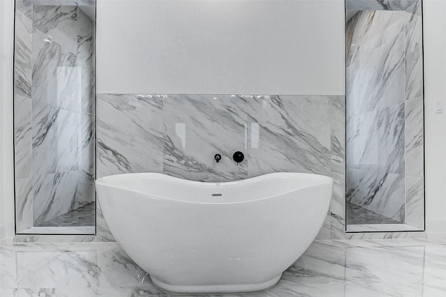 full bath with tile walls, a freestanding tub, and marble finish floor