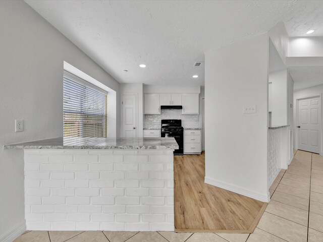 403 Elder Vista Dr, Houston, TX 77598 - kitchen with white cabinets, a peninsula, black gas stove, light stone counters, and under cabinet range hood