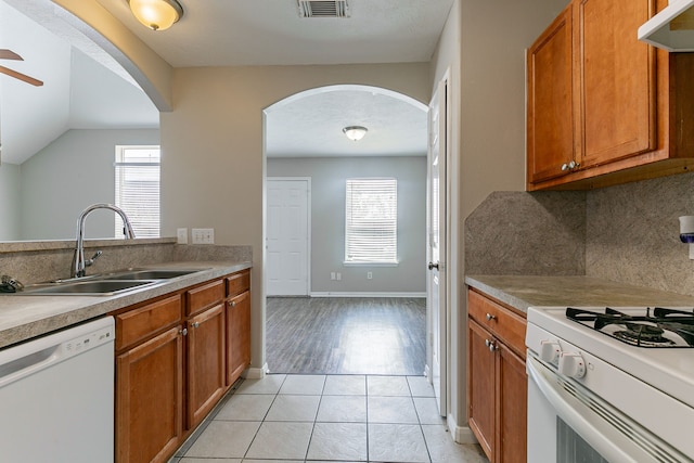 kitchen with arched walkways, white appliances, a sink, and brown cabinetry