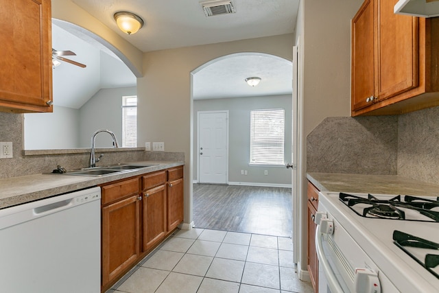 kitchen with arched walkways, a sink, visible vents, white appliances, and brown cabinetry