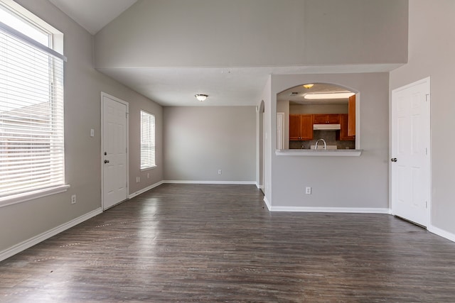unfurnished living room featuring baseboards, dark wood-style floors, arched walkways, and high vaulted ceiling