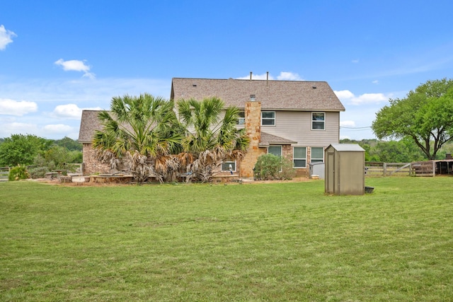 rear view of house with a storage shed, a lawn, an outdoor structure, fence, and roof with shingles