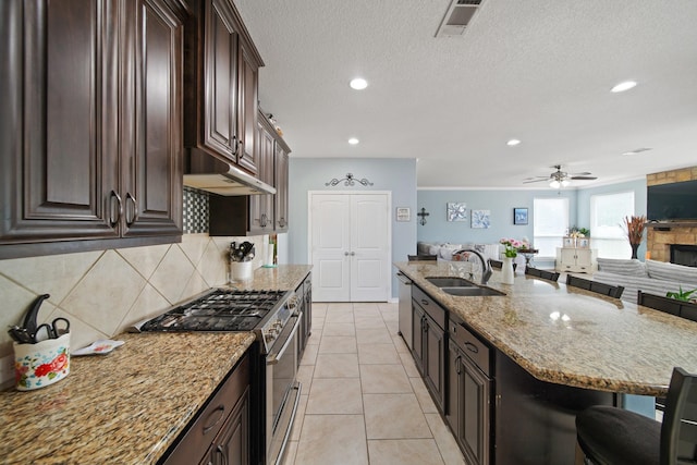 kitchen with under cabinet range hood, light stone countertops, stainless steel appliances, and a sink