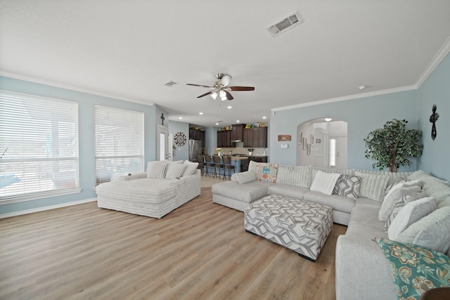 living area with visible vents, a ceiling fan, ornamental molding, arched walkways, and light wood-style flooring