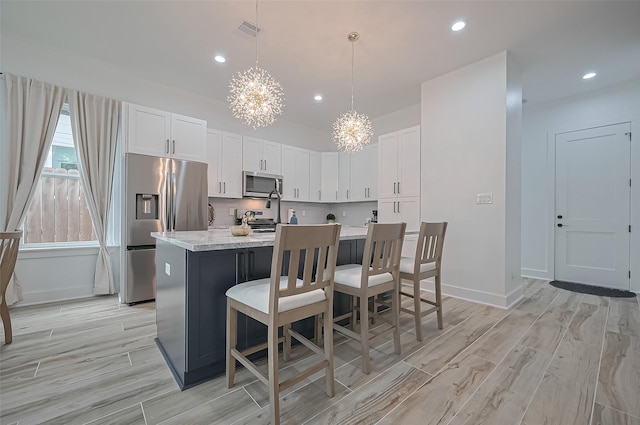kitchen featuring an island with sink, light wood-type flooring, an inviting chandelier, stainless steel appliances, and visible vents