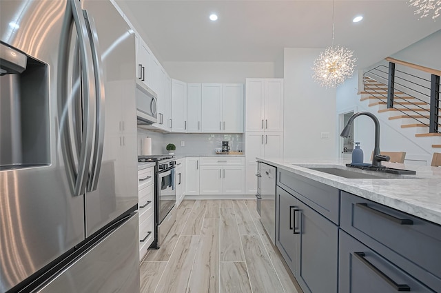 kitchen with stainless steel appliances, light wood-style flooring, a sink, a notable chandelier, and light stone countertops