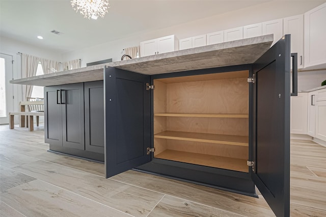 room details featuring white cabinets, a notable chandelier, visible vents, and light wood finished floors