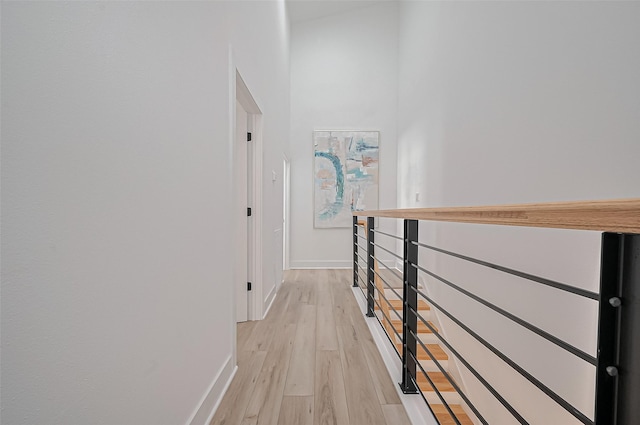 corridor featuring light wood finished floors, baseboards, and a high ceiling