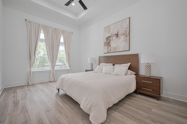 bedroom featuring a ceiling fan, baseboards, light wood-style floors, and a tray ceiling