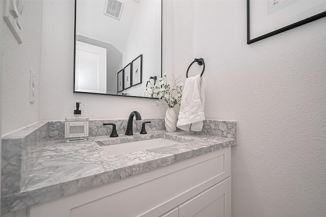 bathroom featuring a textured wall, vanity, and visible vents