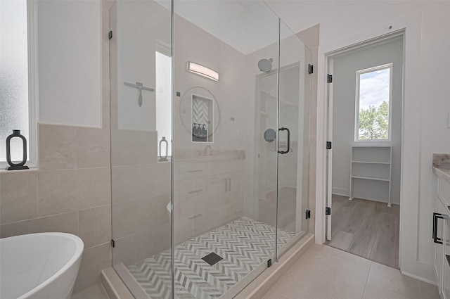 full bathroom featuring tile patterned floors, tile walls, a freestanding tub, a shower stall, and vanity
