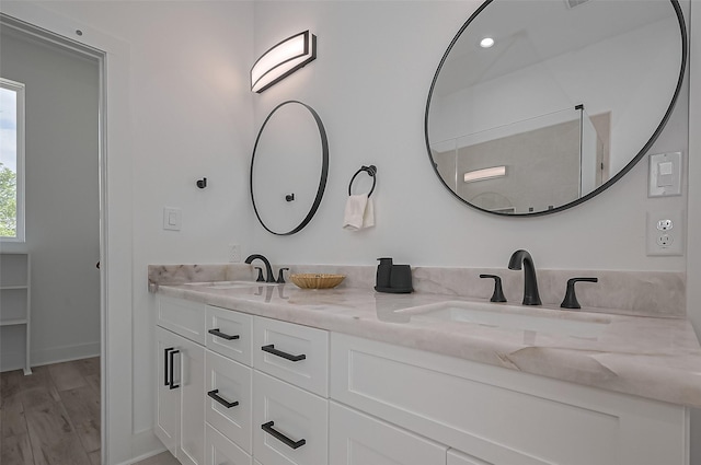 full bath with baseboards, wood finished floors, a sink, and double vanity