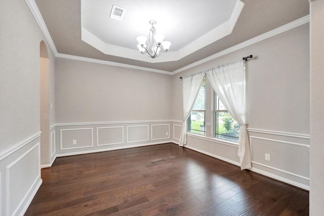 empty room with a raised ceiling, wood finished floors, visible vents, crown molding, and a notable chandelier