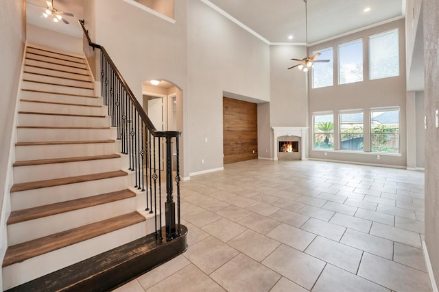 unfurnished living room with stairway, a high ceiling, crown molding, baseboards, and ceiling fan