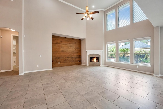 unfurnished living room with a ceiling fan, light tile patterned floors, arched walkways, a premium fireplace, and a high ceiling