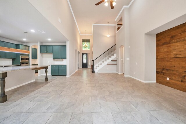 unfurnished living room with stairway, a towering ceiling, visible vents, baseboards, and ceiling fan