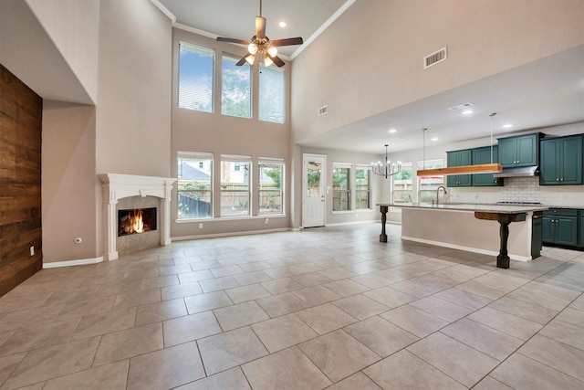 unfurnished living room featuring a sink, visible vents, ceiling fan with notable chandelier, a high ceiling, and a lit fireplace
