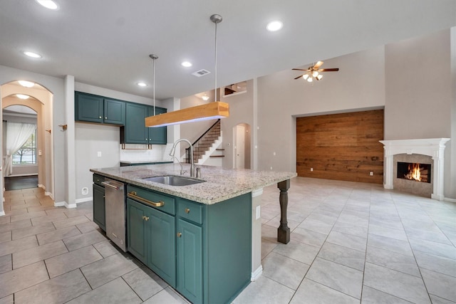 kitchen featuring arched walkways, a sink, a warm lit fireplace, ceiling fan, and an island with sink