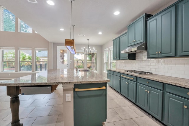 kitchen with a sink, stainless steel gas cooktop, an island with sink, under cabinet range hood, and visible vents