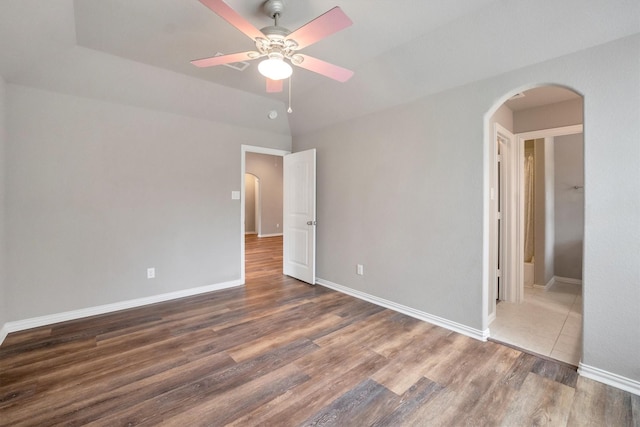 unfurnished bedroom featuring baseboards, wood finished floors, and arched walkways