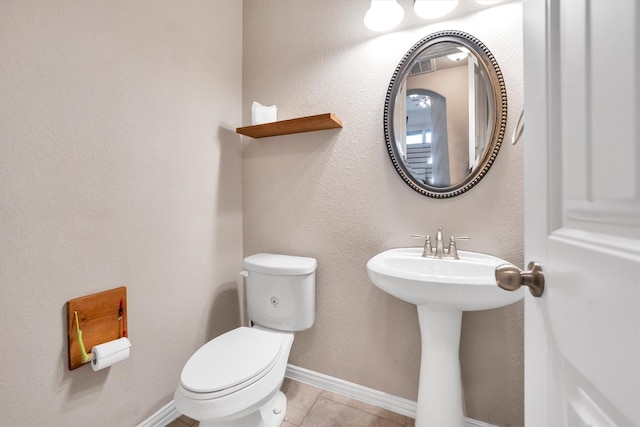 half bathroom featuring baseboards, tile patterned flooring, a sink, and toilet