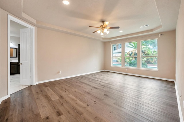 spare room with a raised ceiling, wood finished floors, visible vents, a ceiling fan, and baseboards