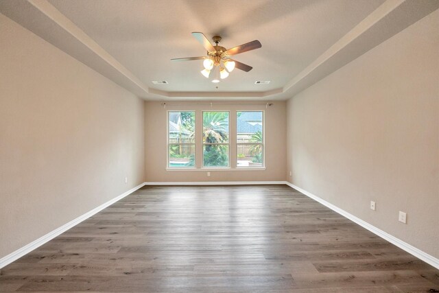 spare room with ceiling fan, wood finished floors, a tray ceiling, and visible vents