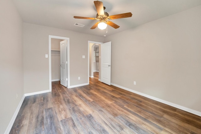 unfurnished bedroom with a closet, wood finished floors, a spacious closet, and baseboards