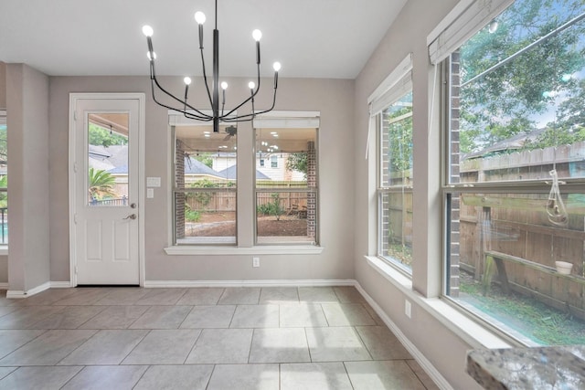 unfurnished dining area with a chandelier, plenty of natural light, tile patterned flooring, and baseboards