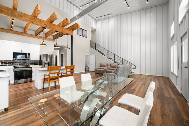 dining area featuring track lighting, wood finished floors, a high ceiling, and stairs