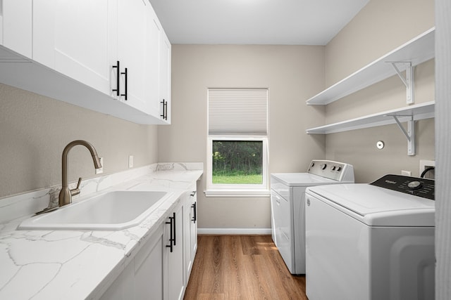 clothes washing area with washing machine and clothes dryer, a sink, baseboards, wood finished floors, and cabinet space