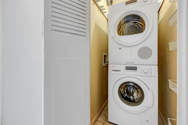 washroom with stacked washing maching and dryer, tile patterned floors, baseboards, and laundry area