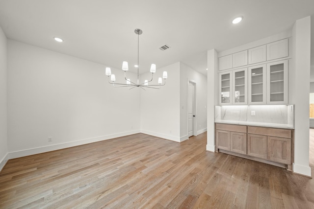 unfurnished dining area featuring an inviting chandelier, baseboards, light wood-type flooring, and visible vents