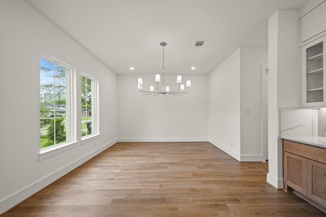 unfurnished dining area featuring an inviting chandelier, light wood-type flooring, recessed lighting, and visible vents