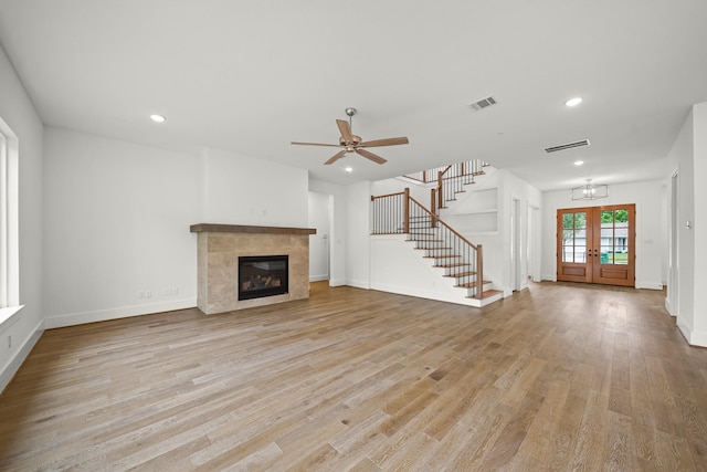unfurnished living room with light wood finished floors, stairs, a tile fireplace, and visible vents