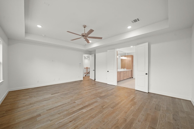 unfurnished bedroom featuring visible vents, a raised ceiling, baseboards, light wood finished floors, and ensuite bathroom