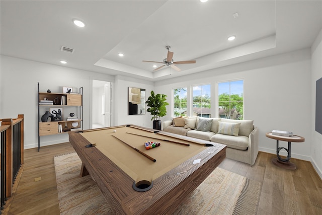 rec room featuring wood finished floors, baseboards, ceiling fan, recessed lighting, and a tray ceiling