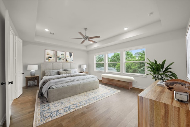 bedroom with baseboards, recessed lighting, a tray ceiling, and wood finished floors
