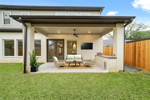 rear view of property featuring ceiling fan, fence, an outdoor hangout area, brick siding, and a yard