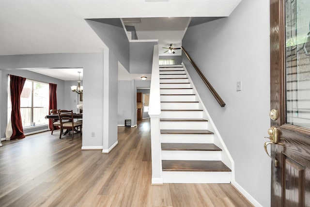 stairway featuring baseboards, wood finished floors, and ceiling fan with notable chandelier